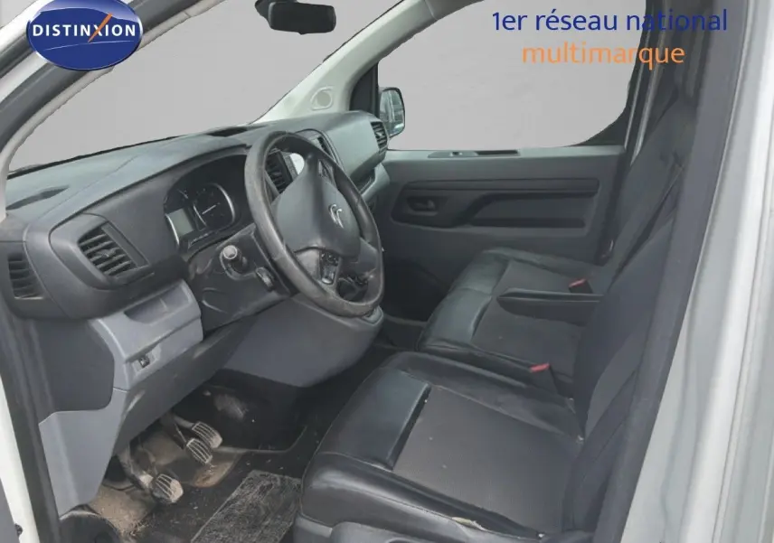 Vue intérieure côté conducteur du Citroën Jumpy blanc, montrant le volant, tableau de bord et sièges noirs en cuir.