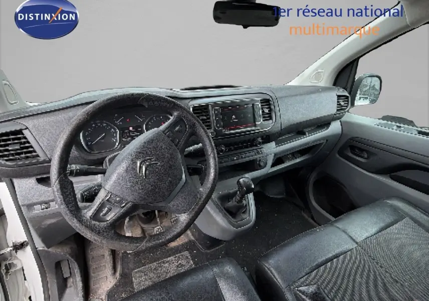 Vue intérieure du poste de conduite du Citroën Jumpy blanc, montrant le volant, tableau de bord et levier de vitesses manuel.