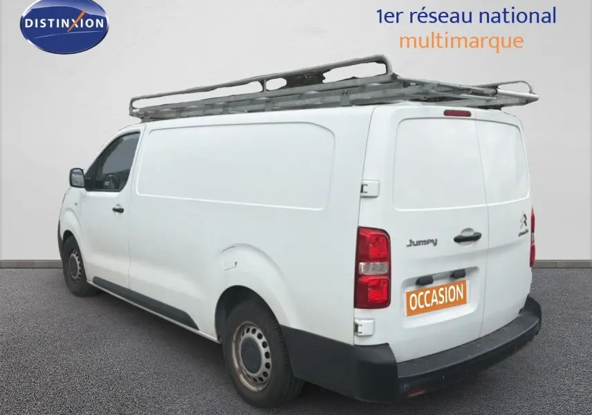 Vue 3/4 arrière gauche d’un utilitaire Citroën Jumpy blanc avec galerie de toit et marquage « Occasion ».