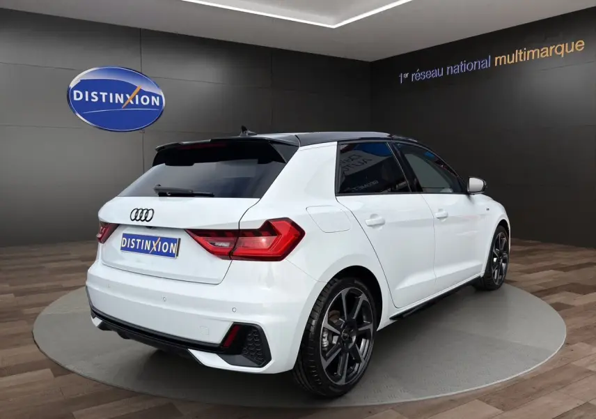 Audi A1 Sportback blanc vue 3/4 arrière droit, avec toit noir et jantes alliage foncé, en showroom.