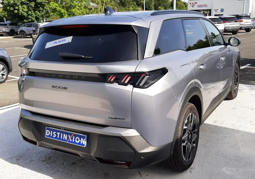 Vue 3/4 arrière droite d’un Peugeot 5008 Hybrid gris Artense métal avec vitres teintées et feux arrière à LED distinctifs.