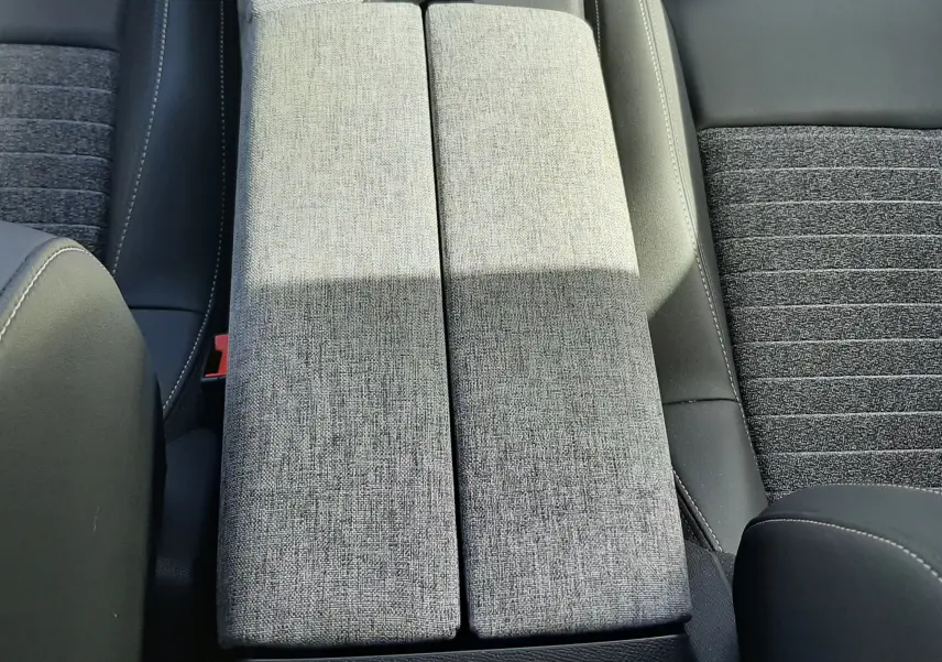 Vue plongeante sur l'accoudoir central gris clair et les sièges tissu gris foncé du Peugeot 5008 Hybrid 2025.