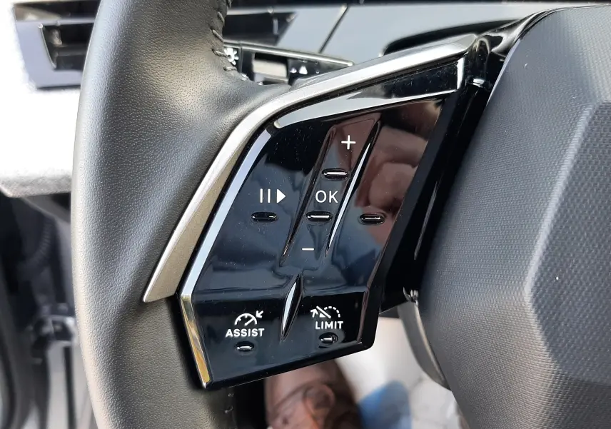Gros plan sur les commandes gauche du volant noir du Peugeot 5008 Hybrid 2025, avec boutons d’assistance et limitation de vitesse.