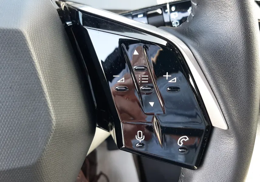 Gros plan sur les commandes tactiles noires à gauche du volant du Peugeot 5008 gris Artense 2025 hybride.