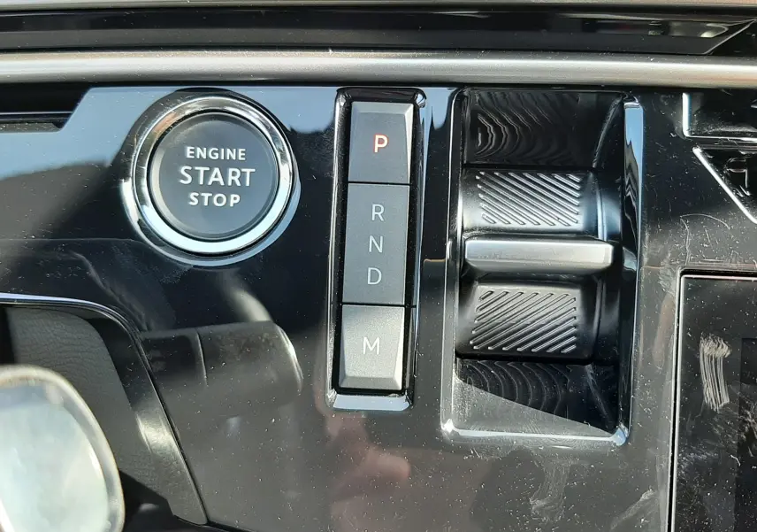 Gros plan sur la console centrale noire brillante du Peugeot 5008 Hybrid 2025, avec bouton start/stop et sélecteur de vitesses automatique.