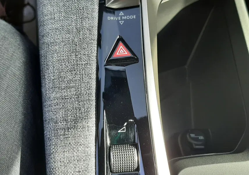 Gros plan sur la console centrale du Peugeot 5008 Hybrid 2025, avec bouton triangle rouge de signalisation et molette Drive Mode.