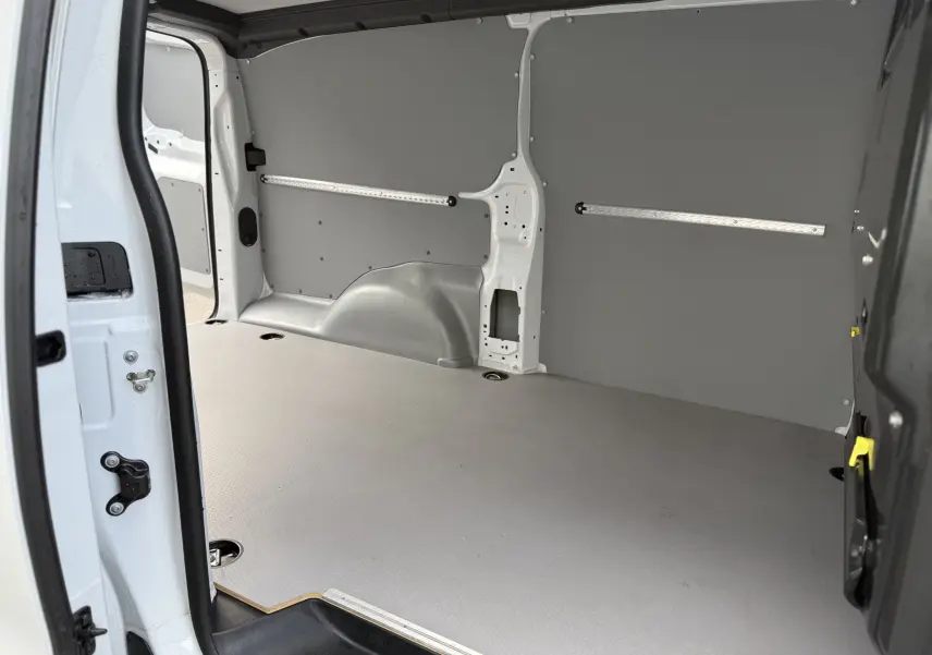 Intérieur du coffre du FIAT Scudo Fourgon blanc Icy, vue depuis la porte latérale ouverte, avec revêtement gris et fixations au sol.