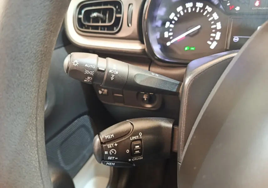 Gros plan sur la commande de régulateur de vitesse et des feux, tableau de bord partiellement visible d'une Citroën C3 2024.
