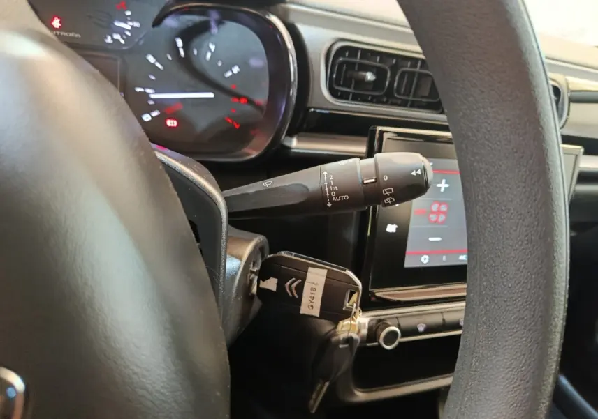 Vue intérieure rapprochée du volant et du tableau de bord d'une Citroën C3 gris foncé avec écran tactile et clé insérée.