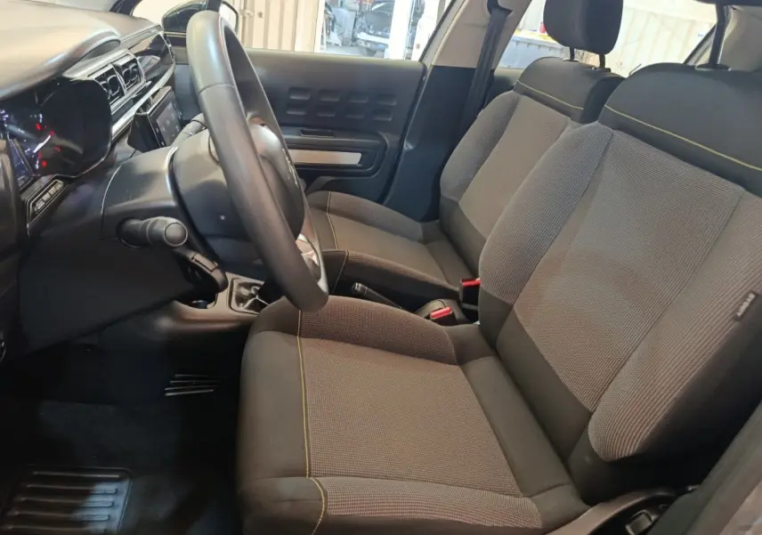 Vue intérieure côté conducteur de la Citroën C3 2024, sièges gris foncé avec surpiqûres jaunes et tableau de bord moderne.