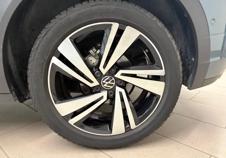 Gros plan sur la roue avant droite du Volkswagen T-Roc bleu pétrole, avec jante alliage bicolore et logo VW central.