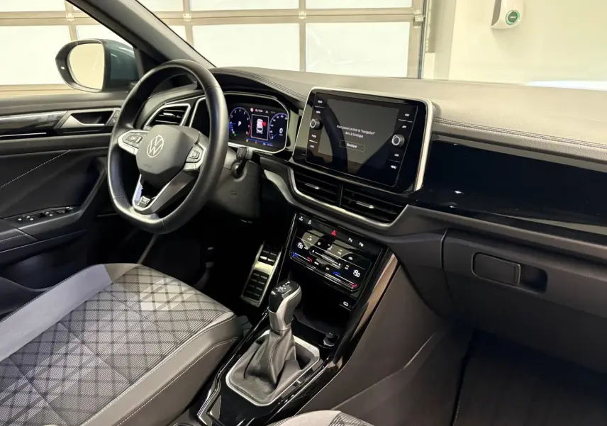 Intérieur du Volkswagen T-Roc 2024 vu côté conducteur, avec tableau de bord numérique et sellerie tissu gris à motifs.