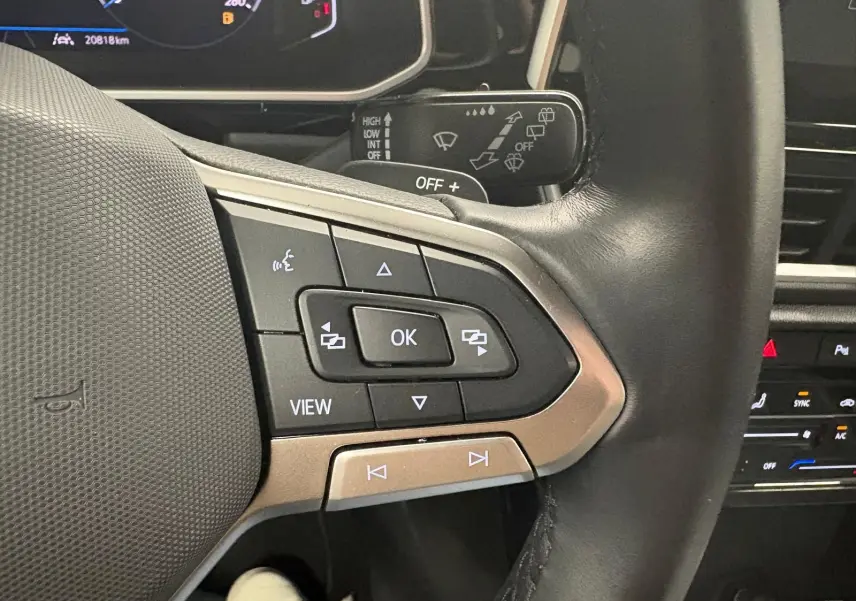 Gros plan sur les commandes gauche du volant cuir du Volkswagen T-Roc 2024 bleu pétrole avec affichage numérique.