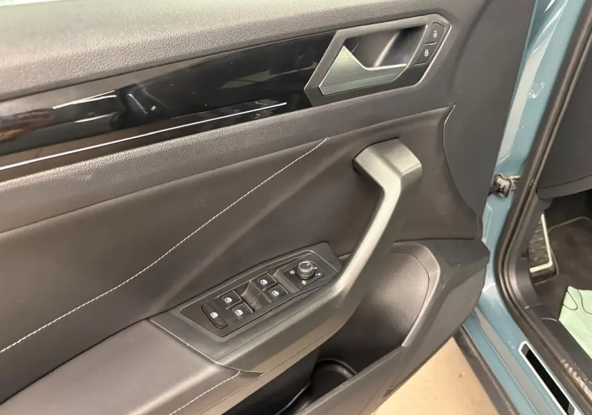 Détail de la porte avant gauche du Volkswagen T-Roc bleu pétrole 2024 avec commandes de vitres et serrure intégrées.