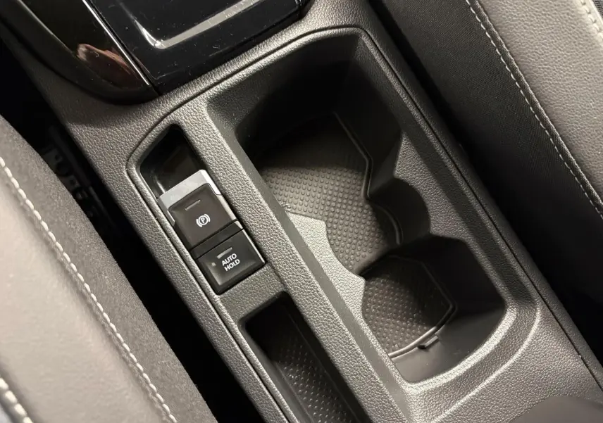 Gros plan sur la console centrale du Volkswagen T-Roc 2024, montrant les porte-gobelets et les commandes de frein à main électrique.