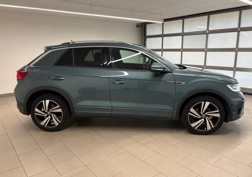 Volkswagen T-Roc 2024 bleu pétrole vu de profil côté gauche avec jantes R-Line et vitres teintées.