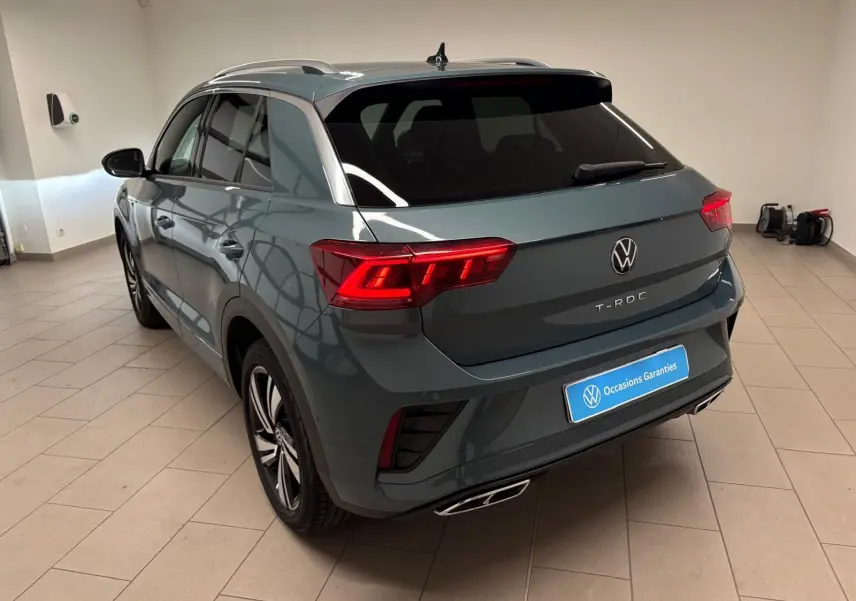 Volkswagen T-Roc bleu pétrole en 3/4 arrière droit, avec feux LED Matrix et finition R-Line visible en intérieur.