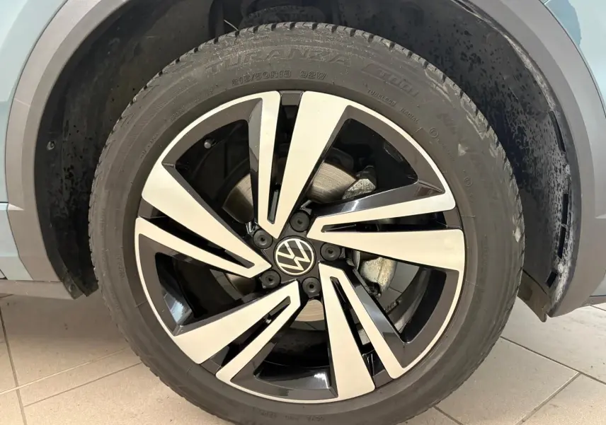 Gros plan sur la jante alliage bicolore du Volkswagen T-Roc bleu pétrole, version R-Line 2024, côté roue avant droite.