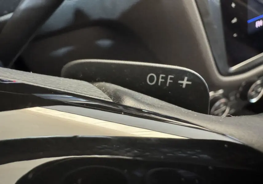 Gros plan sur la palette de changement de vitesse marquée "OFF +" dans l'habitacle du Volkswagen Tiguan Allspace gris foncé.