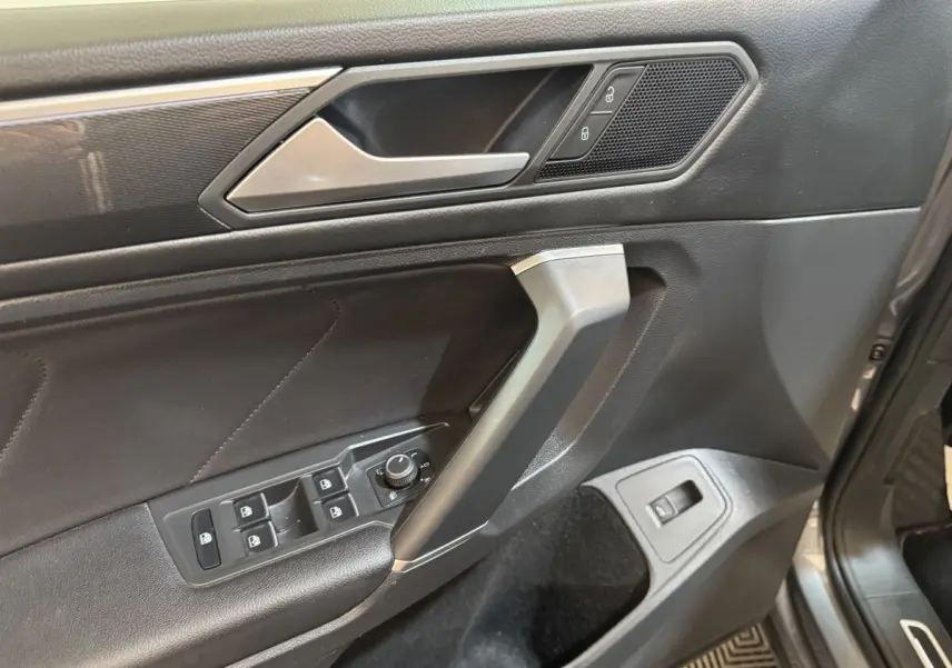 Détail de la porte avant gauche intérieure du Volkswagen Tiguan Allspace gris foncé, avec commandes des vitres et verrouillage.