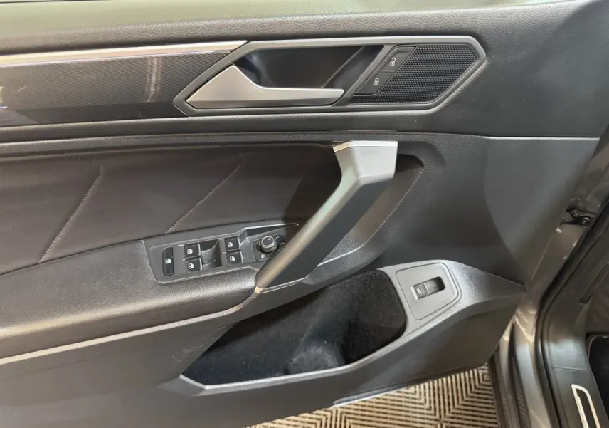 Vue rapprochée de la porte avant gauche du Volkswagen Tiguan Allspace gris foncé, avec commandes de vitres et poignée argentée.