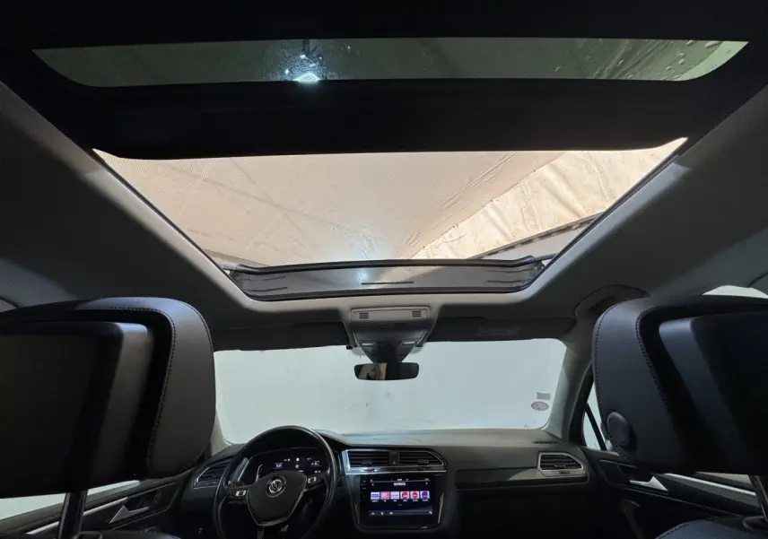 Vue intérieure avant du Volkswagen Tiguan Allspace gris foncé, avec toit ouvrant panoramique et tableau de bord moderne.