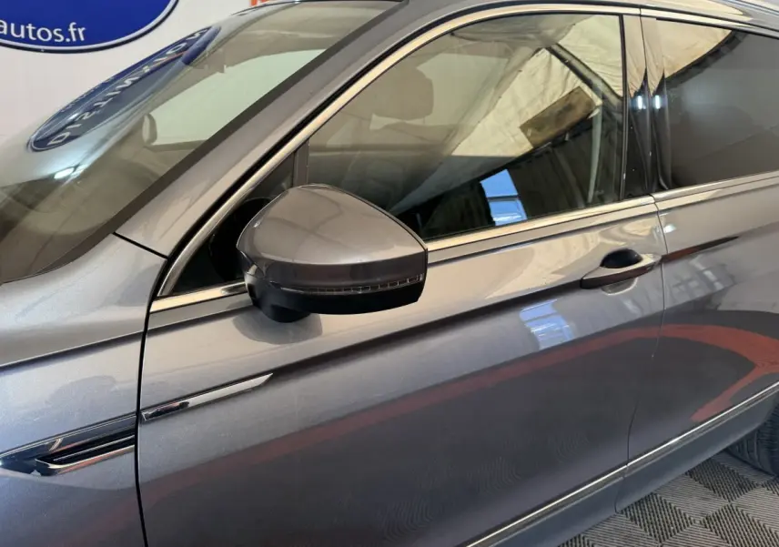 Vue latérale côté gauche du Volkswagen Tiguan Allspace gris foncé, mettant en valeur la ligne de porte et le rétroviseur avec clignotant intégré.