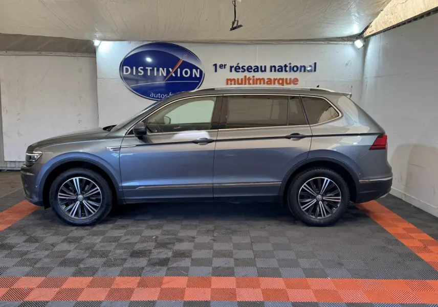 Vue de profil côté gauche d'un Volkswagen Tiguan Allspace gris foncé avec jantes alliage, dans un showroom intérieur.