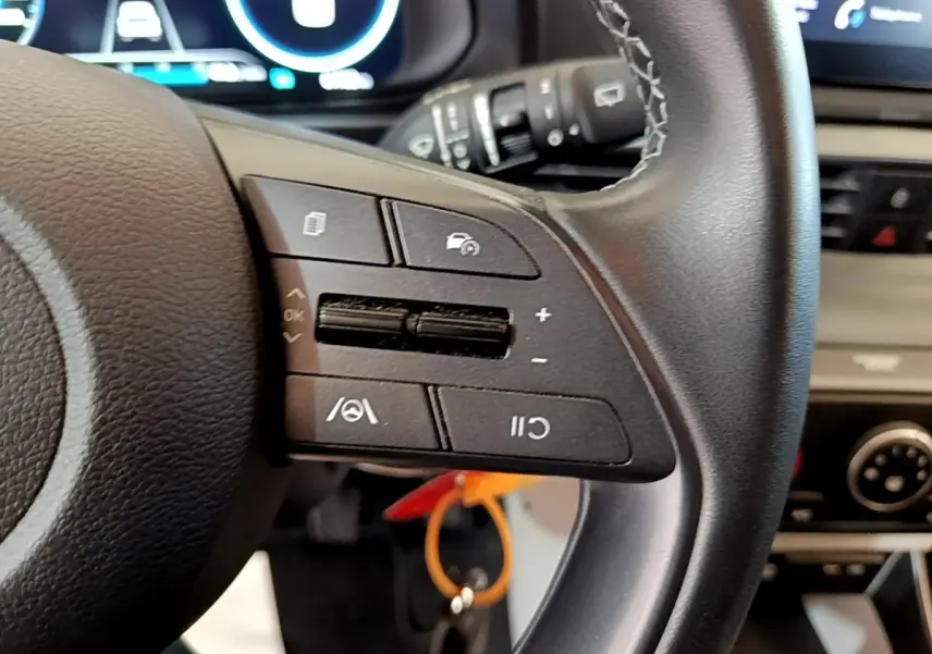 Gros plan sur le volant cuir multifonctions côté gauche de la Hyundai i20 gris clair avec tableau de bord numérique en arrière-plan.