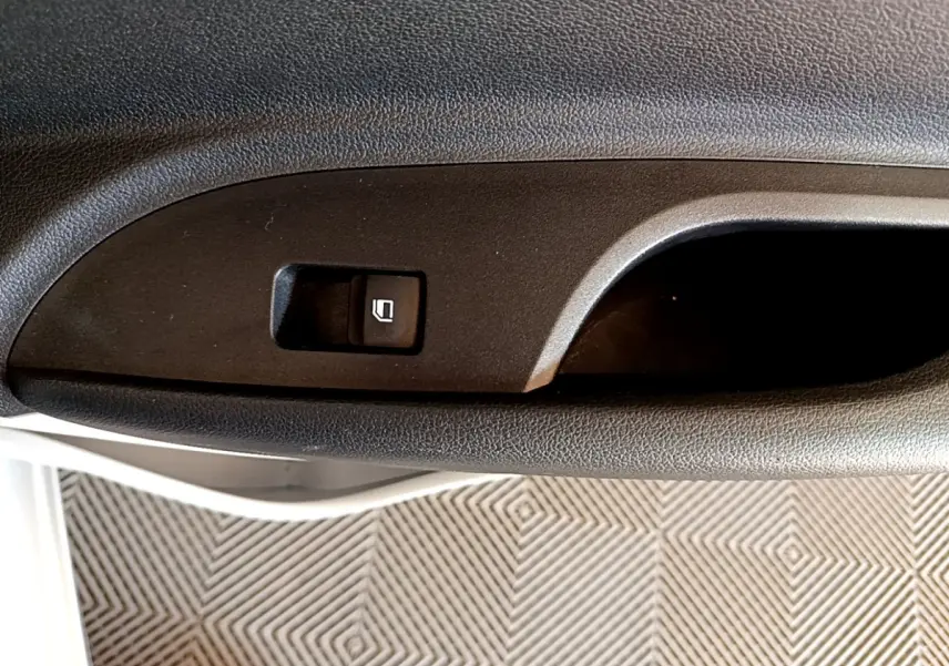 Gros plan sur le bouton de commande de la vitre électrique côté conducteur, intérieur noir texturé.