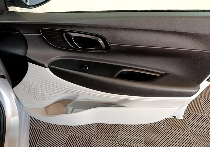 Vue intérieure côté gauche de la porte avant d’une Hyundai i20 gris clair avec poignée noire et panneau bicolore.