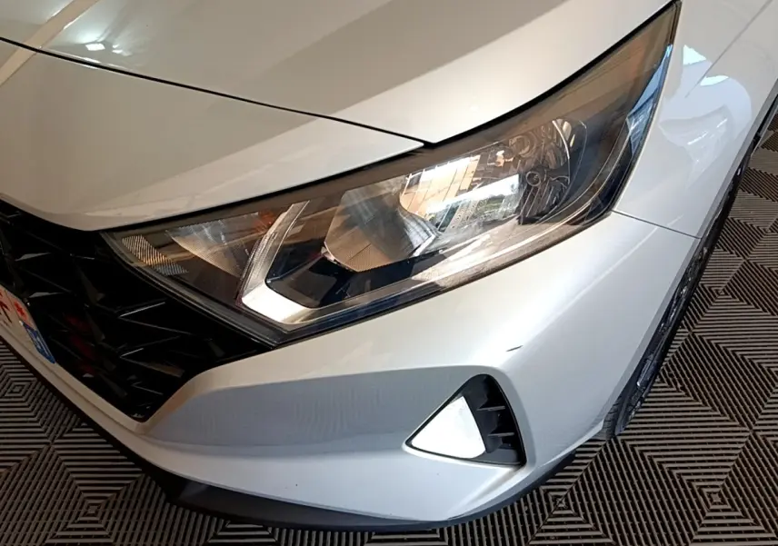 Gros plan sur l'avant droit gris clair de la Hyundai i20 2022 avec phare et calandre noire en losange.