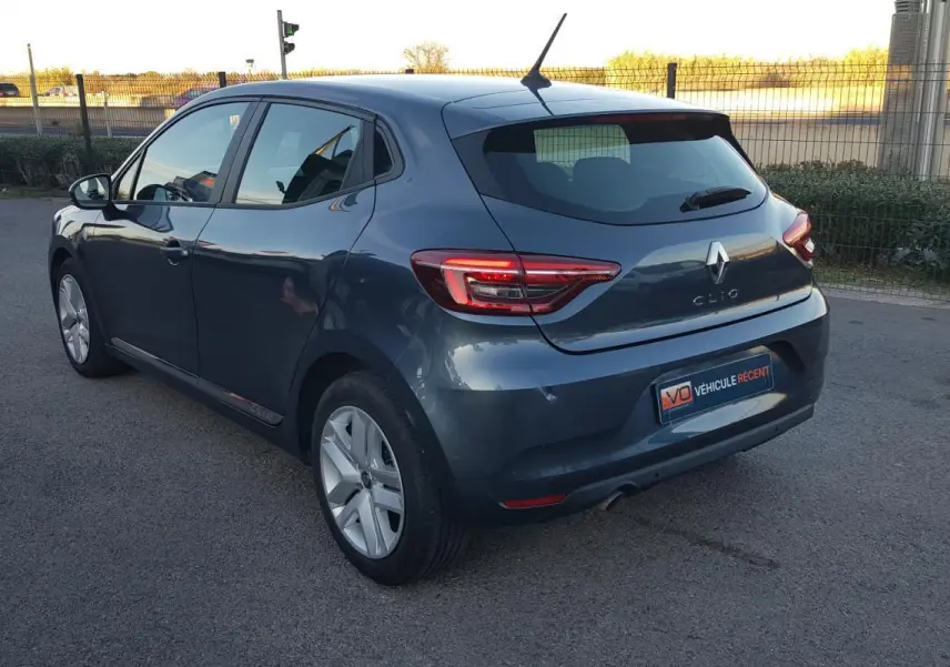Renault Clio gris vue 3/4 arrière droit, avec feux arrière allumés et jantes alliage visibles.