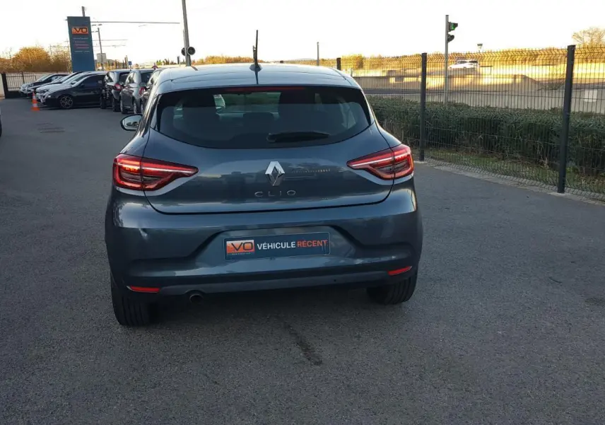 Vue arrière d'une Renault Clio gris foncé 2021, avec feux arrière allumés sur un parking extérieur.