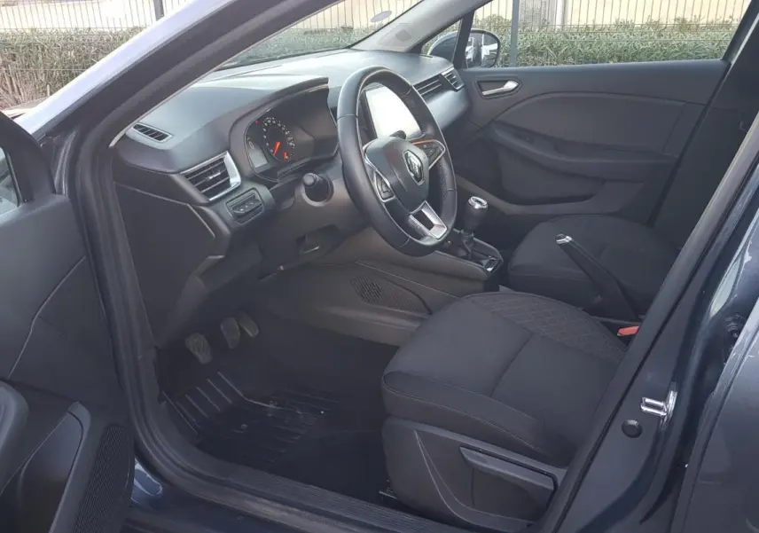 Intérieur côté conducteur d'une Renault Clio gris 2021, montrant le volant, tableau de bord et sièges noirs.