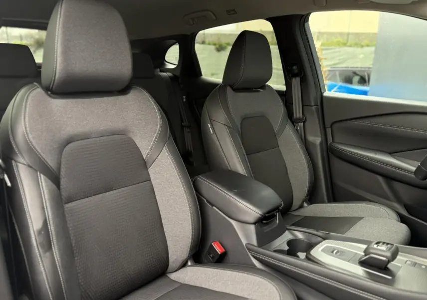 Vue intérieure des sièges avant gris clair et foncé du Nissan Qashqai 2024 avec accoudoir central et console moderne.