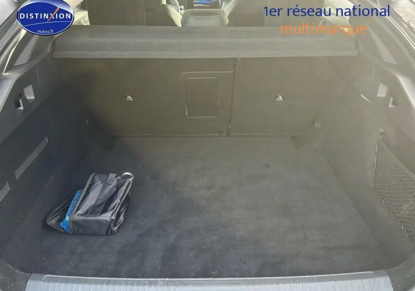 Vue intérieure du coffre spacieux et propre de la Peugeot 408 Hybrid 145 allure gris sélénite avec filet de rangement latéral.