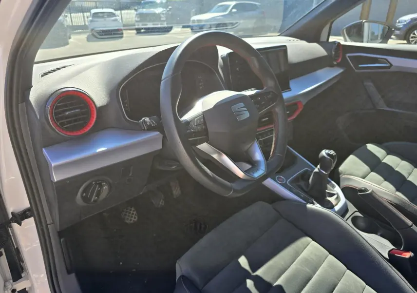 Vue intérieure côté conducteur du SEAT Arona 2024, volant sport cuir noir avec surpiqûres rouges et sellerie suédine noire.