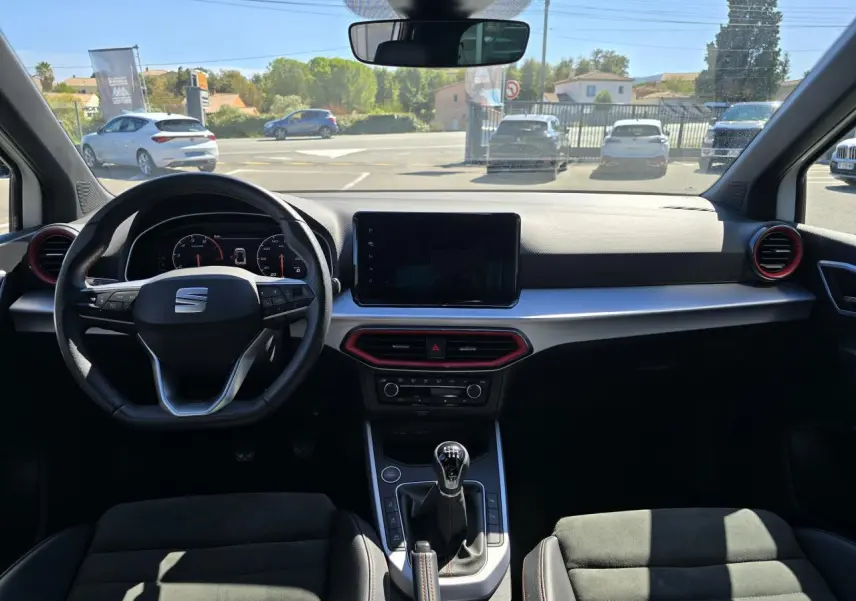 Vue intérieure frontale du tableau de bord du SEAT Arona 2024, volant cuir noir, détails rouges et écran tactile central.