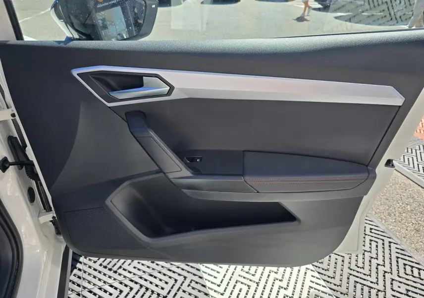 Vue intérieure de la porte avant gauche d'une SEAT Arona 2024 blanc toit noir, avec garniture noire et surpiqûres rouges.