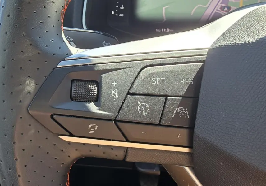 Gros plan sur les commandes du volant en cuir perforé noir avec surpiqûres rouges du SEAT Arona 2024, mode régulateur et aide à la conduite.