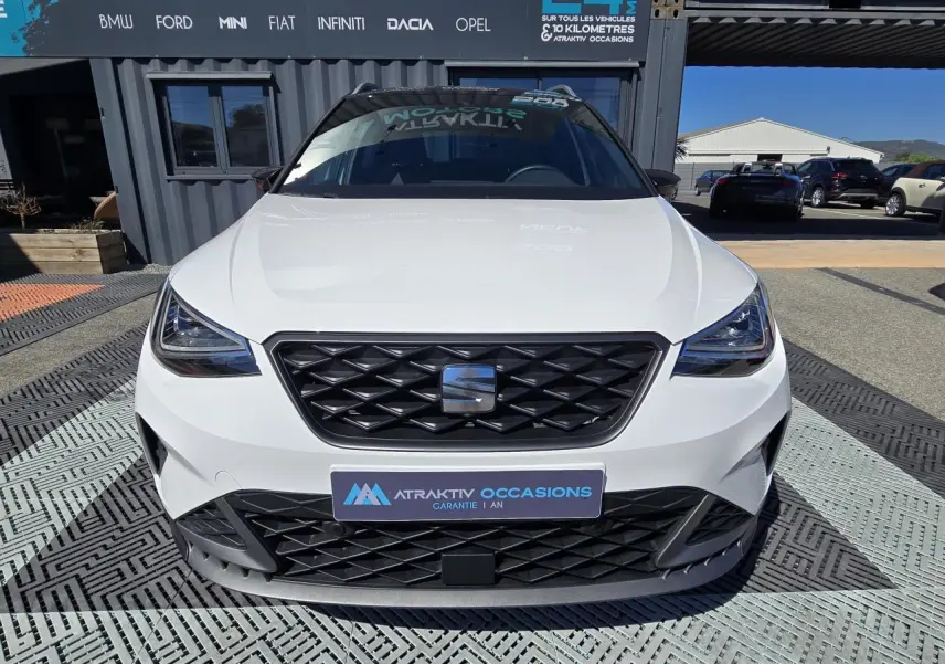 Vue avant d'une SEAT Arona 2024 blanche avec toit noir, calandre spécifique FR et projecteurs Full LED triangulaires.