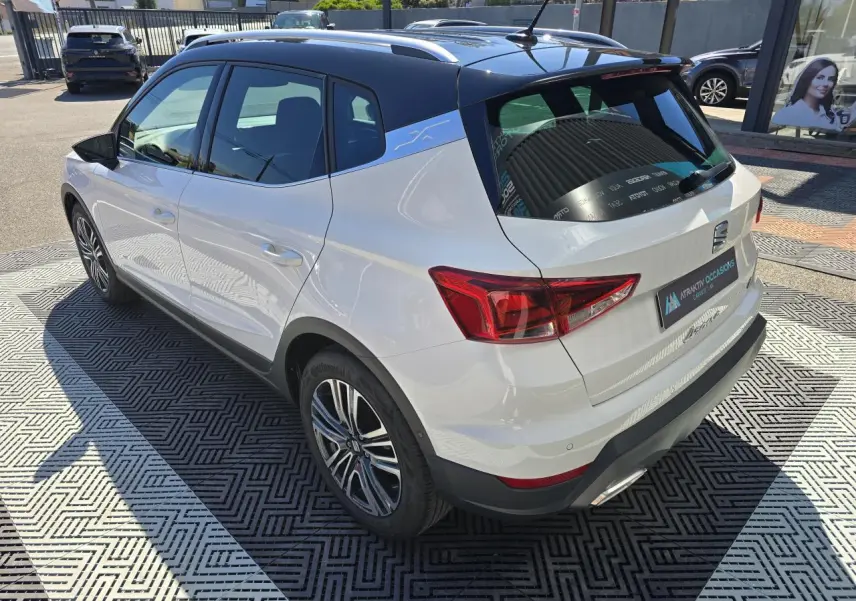 Vue 3/4 arrière droite d'un SEAT Arona blanc avec toit noir et jantes alliage, stationné en extérieur au soleil.