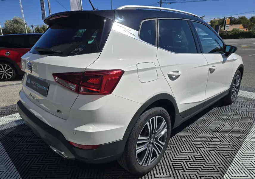 Vue 3/4 arrière droite d'un SEAT Arona blanc avec toit noir et jantes alliage, en extérieur sur parking.