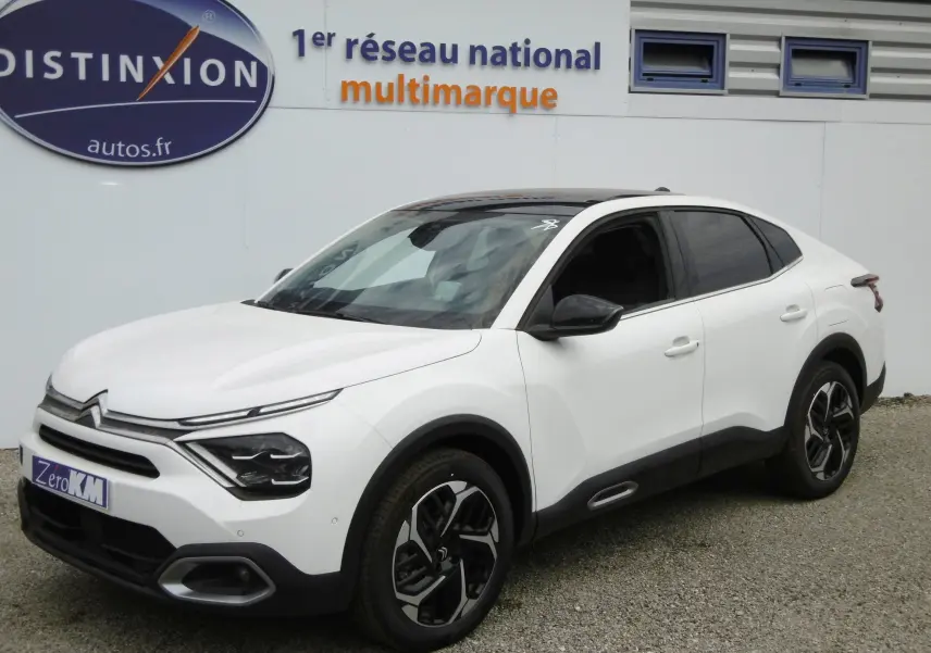 Citroën C4 X blanc polaire en 3/4 avant droit, avec jantes bicolores et vitres teintées sur parking extérieur.