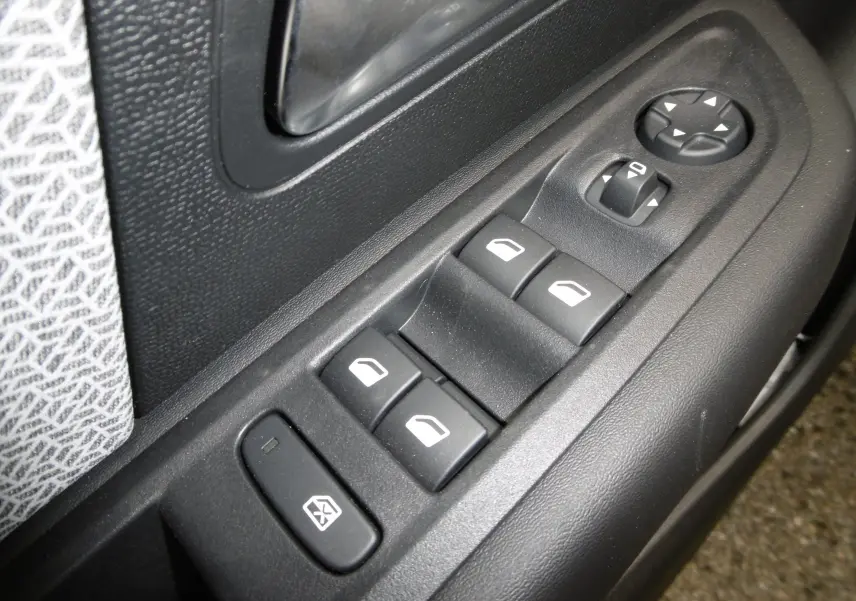 Gros plan sur les commandes de lève-vitres et réglage des rétroviseurs côté conducteur d'une Citroën C4 X blanche.