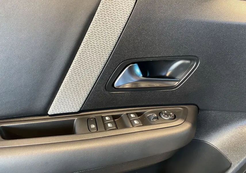 Détail de la porte côté conducteur de la Citroën C4 2023, avec commandes de vitres et poignée argentée sur panneau noir et gris.