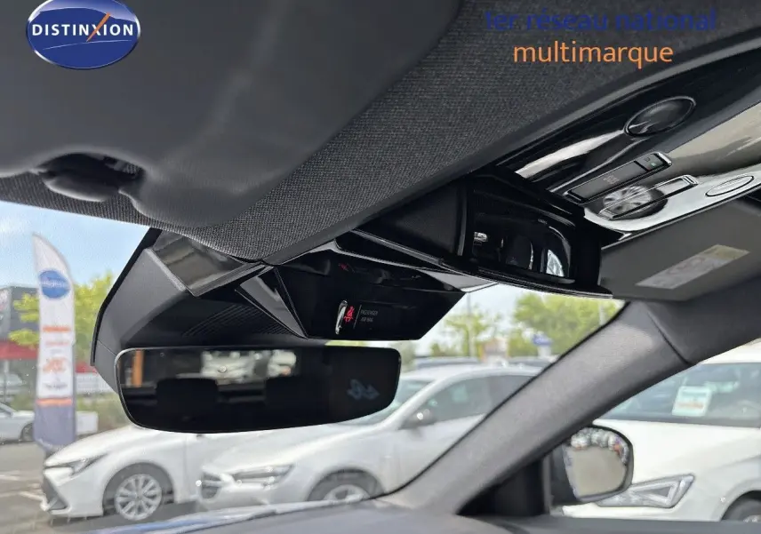 Vue intérieure du rétroviseur central et du plafonnier du Renault Austral bleu iron avec toit noir, en stationnement extérieur.