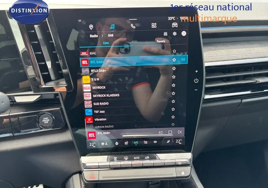 Vue rapprochée de l'écran tactile central du Renault Austral 2024 bleu iron, affichant les stations radio avec commandes climatisation en dessous.