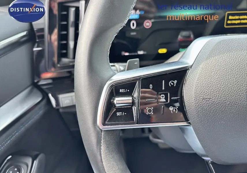 Gros plan sur les commandes à gauche du volant en cuir noir du Renault Austral 2024 hybride, avec tableau de bord numérique en arrière-plan.